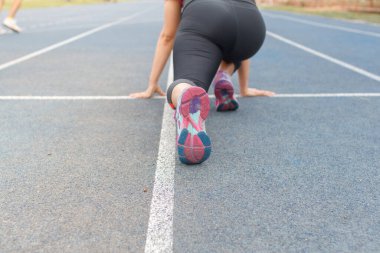 Koşan kadın stadyumdaki mavi pistte poz veriyor.