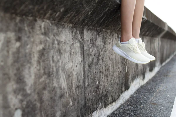 Female is sitting on a wall and hanging the legs