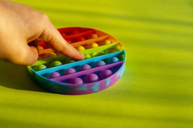Trendy colorful anti-stress sensory toy. Silicone fidget push pop it for fine motoric skills lies in the sun. Flat lay on green background. Picture with place for text.