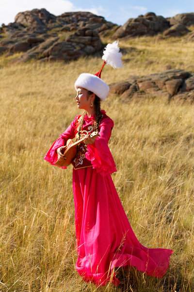 Beautiful kazakh woman in national costume in the steppe dancing with dombyra