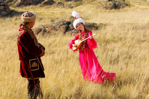 Kazajstán hombre y mujer en trajes nacionales en la estepa jugando dombyra y bailando —  Fotos de Stock