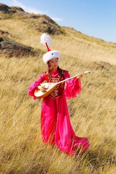 Belle femme kazakh en costume national dans la steppe dansant avec dombyra — Photo