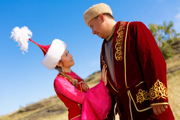 Kazakiska man och kvinna i nationella kostymer i stäppen spelar dombyra och dans — Stockfoto