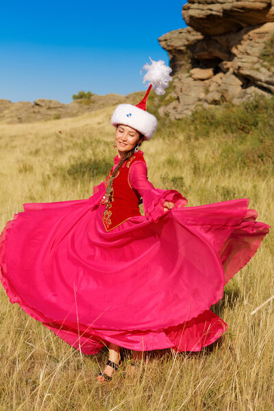 Beautiful kazakh woman in national costume in the steppe dancing with dombyra