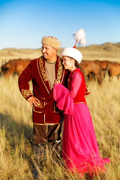 Kazakiska man och kvinna i nationella kostymer i stäppen spelar dombyra och dans — Stockfoto