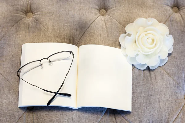 Libro bianco con occhiali rosa candela sul divano — Foto Stock