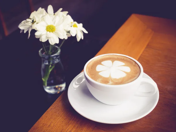 Tazza da caffè con decorazione floreale bianca su tavolo di legno — Foto Stock