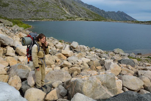 Tourist girl eating snow near a mountain lake on the top of the — Stock Photo, Image