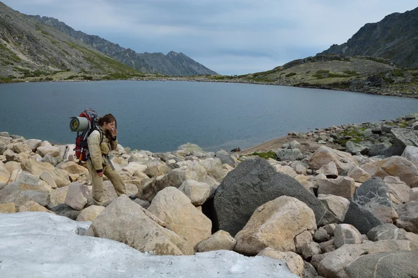 Chica turística comiendo nieve cerca de un lago de montaña en la cima de la — Foto de Stock