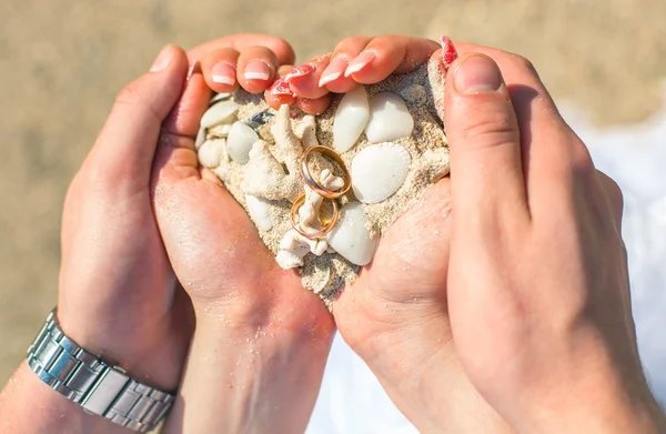 Férfi és nő a gazdaság homok és kagyló coral esküvői gyűrű, a strandon — Stock Fotó