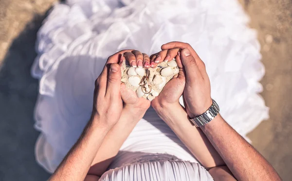 Hombre y mujer sosteniendo arena y conchas de coral con un anillo de bodas en la playa — Foto de Stock