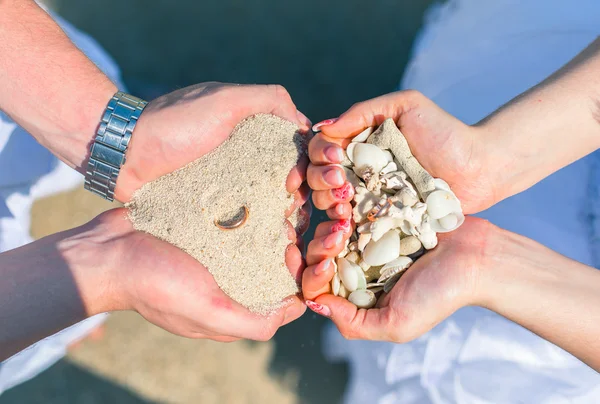 Мужчина и женщина держат в руках песок и раковины кораллов с обручальным кольцом на пляже Стоковое Фото
