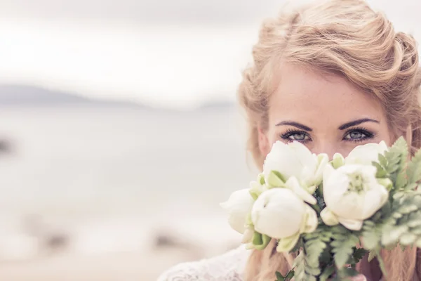 Glücklich schönes Mädchen in einem Hochzeitskleid mit einem Strauß am Meer — Stockfoto