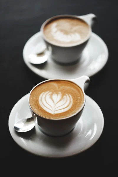 Two cups of cappuccino on black table — Stock Photo, Image