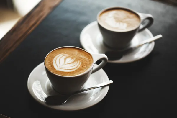 Två koppar cappuccino på svart bord — Stockfoto