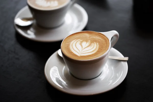 Two cups of cappuccino on black table — Stock Photo, Image