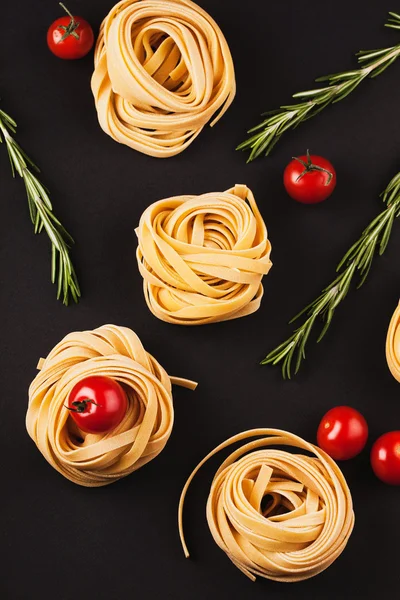 Cherry tomatoes, branches of rosemary and raw pasta on black bac — Stock Photo, Image