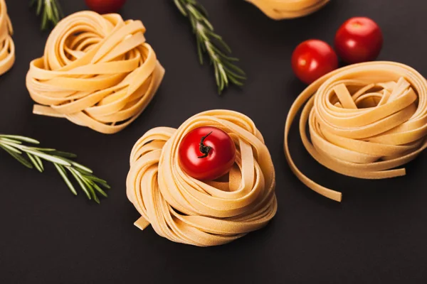 Cherry tomatoes, branches of rosemary and raw pasta on black bac — Stock Photo, Image