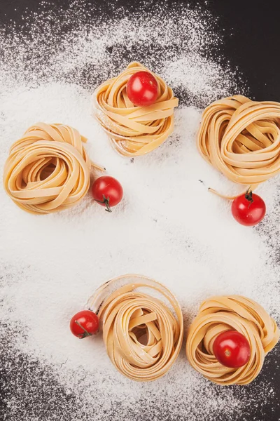 Pasta and tomatoes on flour — Stock Photo, Image