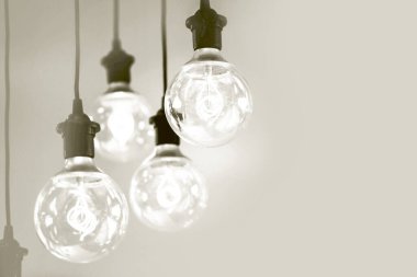 Birden fazla antik stil edison filament ampulleri asılı, arka planda ışıkla parlıyor, ilhamı sembolize ediyor. 2026 'nın beyaz bulutlu dansçısı.