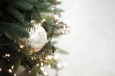 Yeşil suni Noel ağacı dalları parlak altın bir süs eşyası sergiliyor ve ışıklandırılmış ip ışıkları yakıyor, bayram atmosferi yaratıyor. 2026 'nın beyaz bulutlu dansçısı.