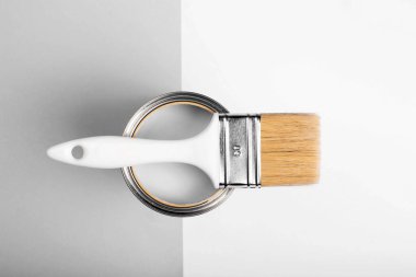 Boya fırçası açık bir boya kutusunda duruyor, gri ve beyaz yüzeyler zıt bir perspektif oluşturuyor. 2026 'nın beyaz bulutlu dansçısı.