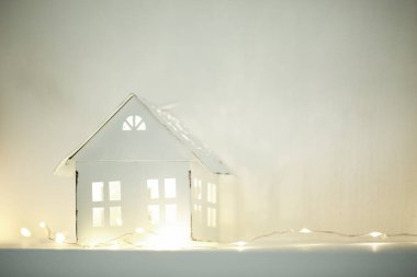 Beyaz kağıt ev modeli, festival ışıklarıyla parıldıyor. Kış tatili için samimi, sıcak ve davetkar bir atmosfer yaratıyor. 2026 'nın beyaz bulutlu dansçısı.