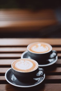 İki gri kapuçino ve ahşap masa üzerinde latte sanatı..