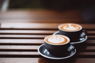 İki gri kapuçino ve ahşap masa üzerinde latte sanatı..