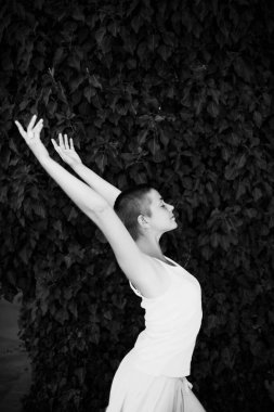 Kısa saçlı, açık renk elbiseli, kollarını yukarı doğru uzatan, özgürlük, maneviyat ve refah kavramlarını somutlaştıran, yemyeşil yaprakların zeminine karşı olan bir kadın.