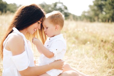Sevgi dolu bir anne, güneşli bir tarlada oturur ve oğullarını açık havada keşfederken yanında tutar. Hakiki aile bağı, özen ve günlük mutluluk doğada esir alınmıştır..