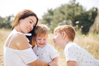 Sevgi dolu bir anne, güneşli bir kırsal bölgede güneşli bir günde, günlük aile bağlarını, bakımlarını ve mutluluklarını yakalayarak, iki küçük oğlunu açık havada kucaklıyor..