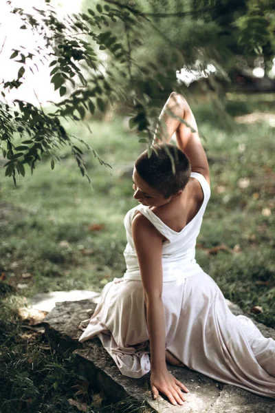 Oturduğu yoga pozu sırasında dengesine ve esnekliğine odaklanan bir kadın yeşil yapraklı sakin bir park ortamında farkındalık ve rahatlama pratiği yapıyor.