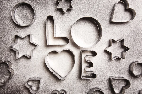 Love shaped cookie cutters and flour on black background — Stock Photo, Image