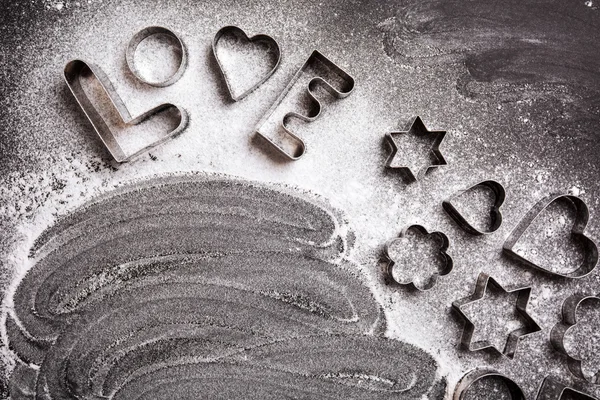 Love shaped cookie cutters and flour on black background — Stock Photo, Image