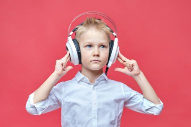 Kulaklık tutan sevimli küçük çocuk elleri başının üstünde kırmızı bir arka planda..