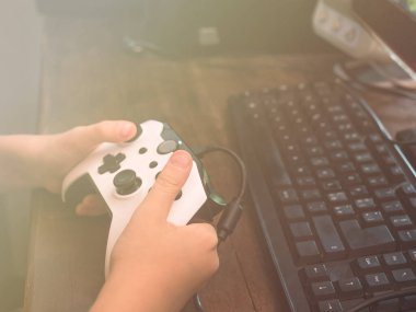 Küçük çocuk bilgisayarın önünde joystickle oynuyor.