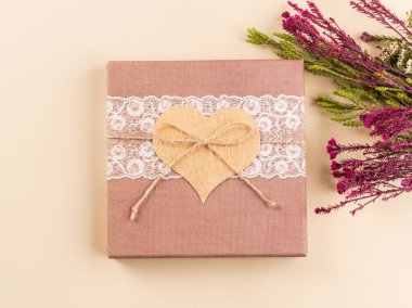 Kalp ve kurumuş çiçeklerle bej bir hediye kutusu.