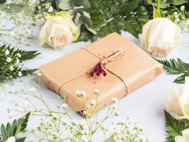 Kurumuş çiçek dekoru ve etrafında güller olan hediye kutusu.