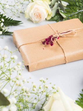 Kurumuş çiçek dekoru ve etrafında güller olan hediye kutusu.