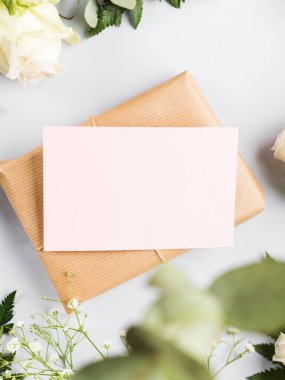 Paketlenmiş hediye kutusu, etrafında pembe kart ve çiçekler var.