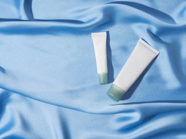 Mavi saten arka planda iki genel krem tüpü, cilt bakımı ürünü görüntüsü