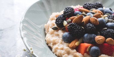 Lezzetli kahvaltılık yulaf lapası. Bitki sütü, fındık ve mermer masada böğürtlen.