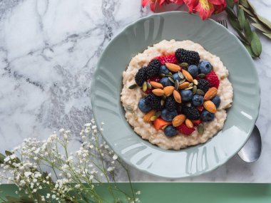 Lezzetli kahvaltılık yulaf lapası. Bitki sütü, fındık ve mermer masada böğürtlen.