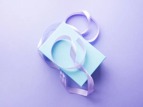 Niebieskie pastelowe pudełko i fioletowa wstążka na fioletowym tle. Pojęcie prezentu wakacyjnego — Zdjęcie stockowe