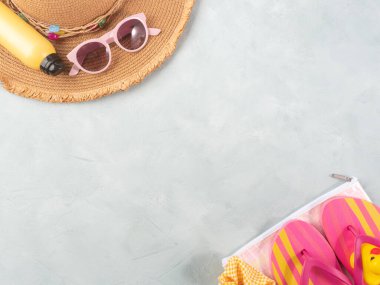 Yaz tatili aksesuarları. Hasır şapka, parmak arası terlik, güneş spreyi, taştan arka planda güneş gözlüğü..
