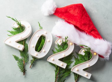 Yeni yıl 2022 numaraları, köknar ağacı dalları ve gri arka planda Noel Baba şapkası. Tatil tebrik kartı.