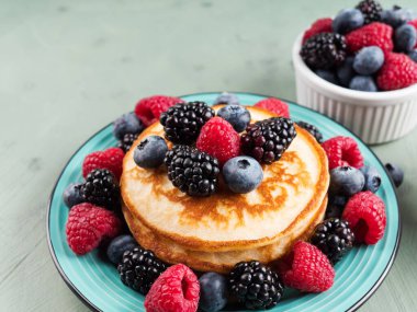 Yeşil arkaplanda servis edilen ahududu ve yaban mersinli krep yığını