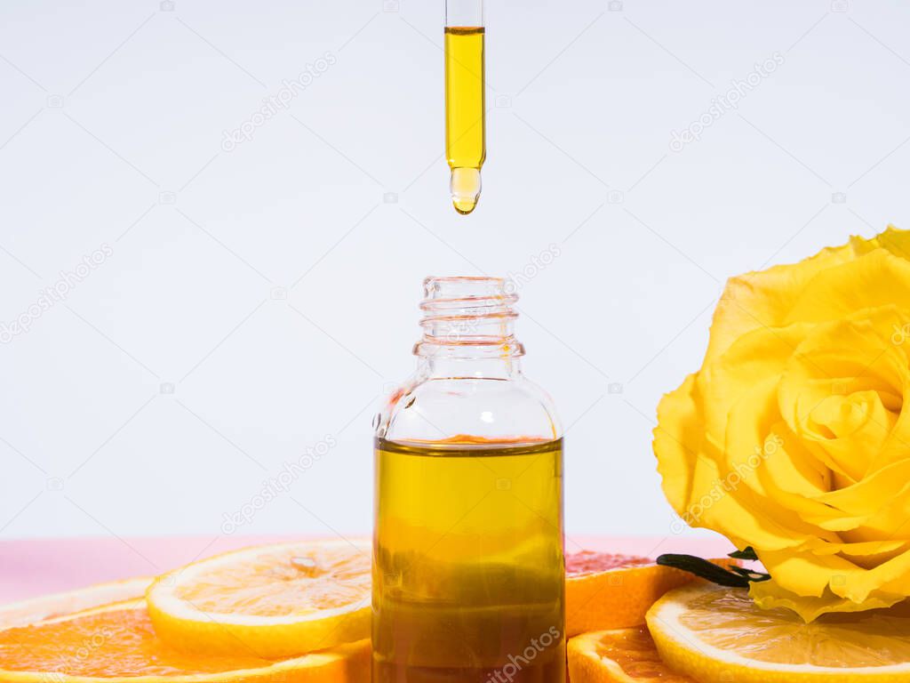 Vitamin C serum bottle with dropper on pink background with orange citrus slices