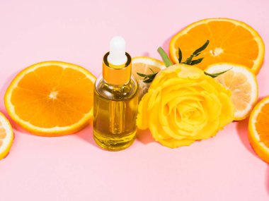 C vitamini serumu şişesi. Pembe arka planda damlatıcı ve turuncu narenciye dilimleri var.